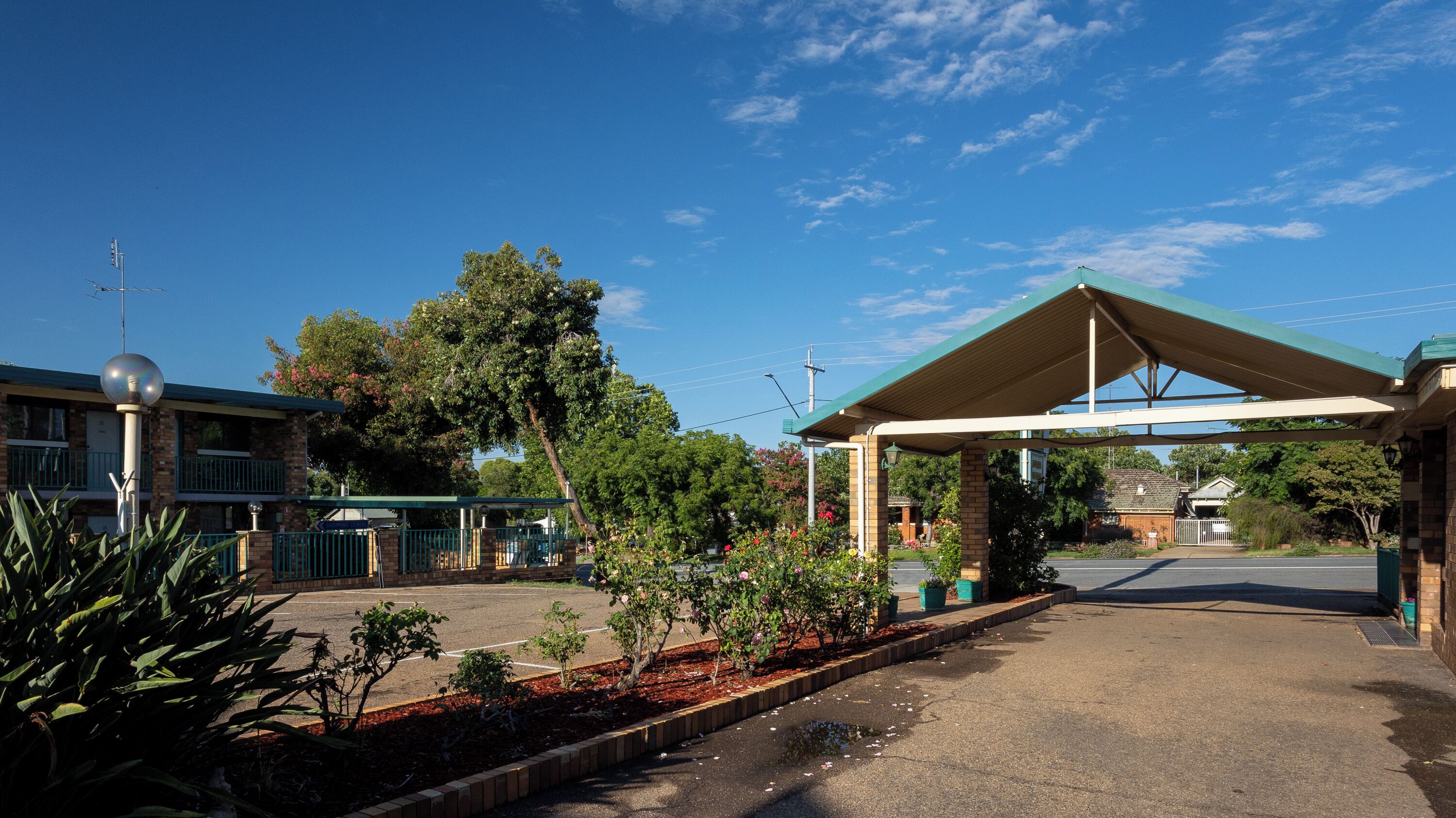 A building with a covered entrance, a parking lot, and surrounding greenery.