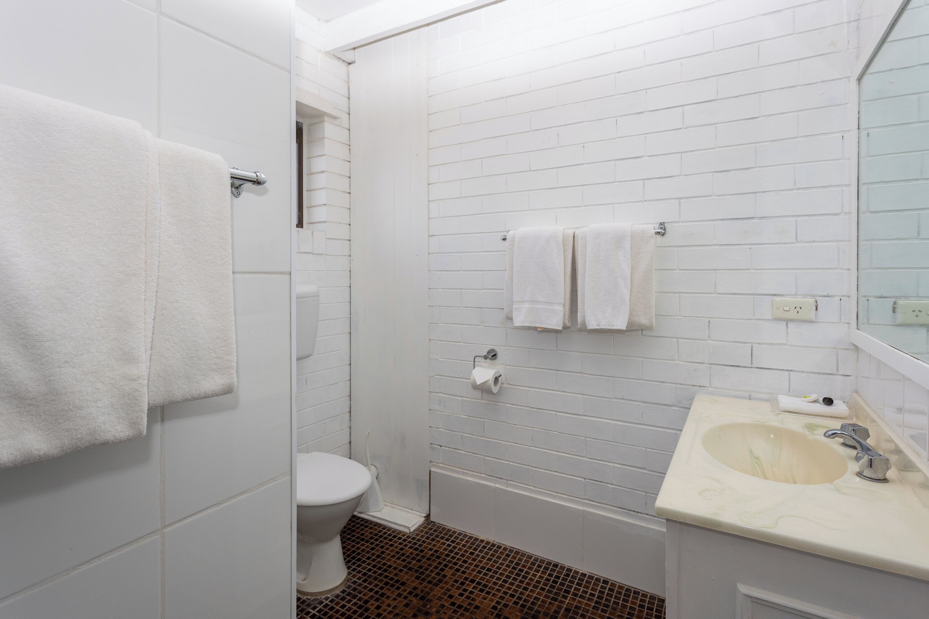 A bathroom with white tiled walls, a white toilet, a bathtub, and a sink with a mirror.
