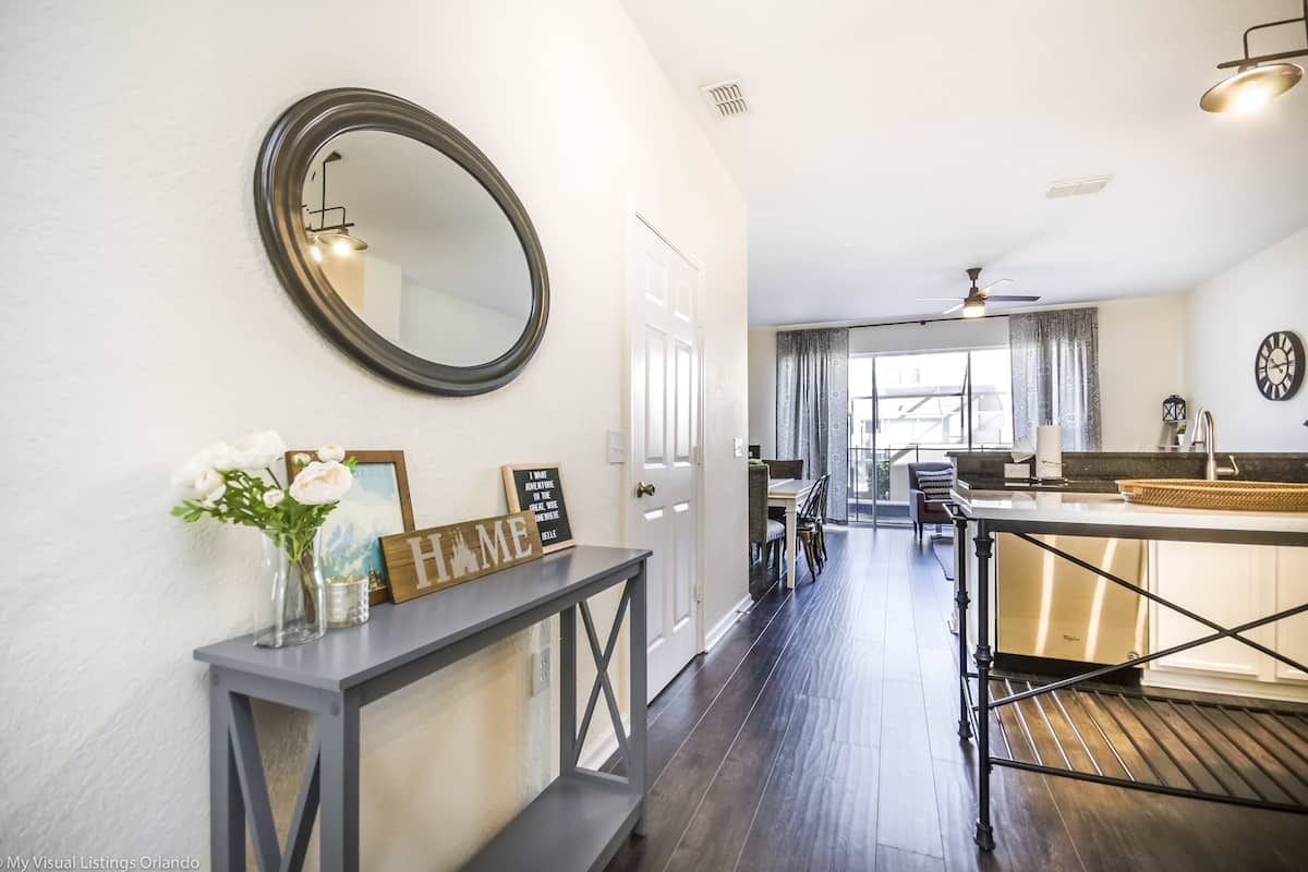A modern kitchen with a dark wood floor, a large round mirror, and a dining area with a table and chairs.