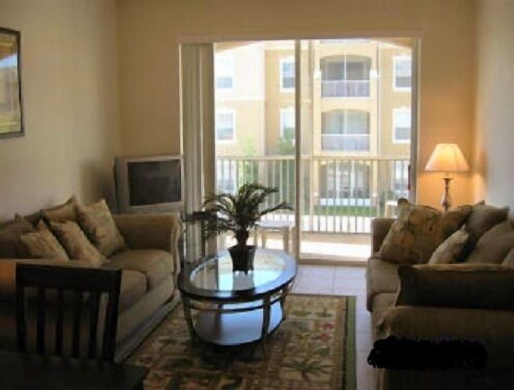A living room with two sofas, a coffee table, a TV, and a balcony with a view of buildings.