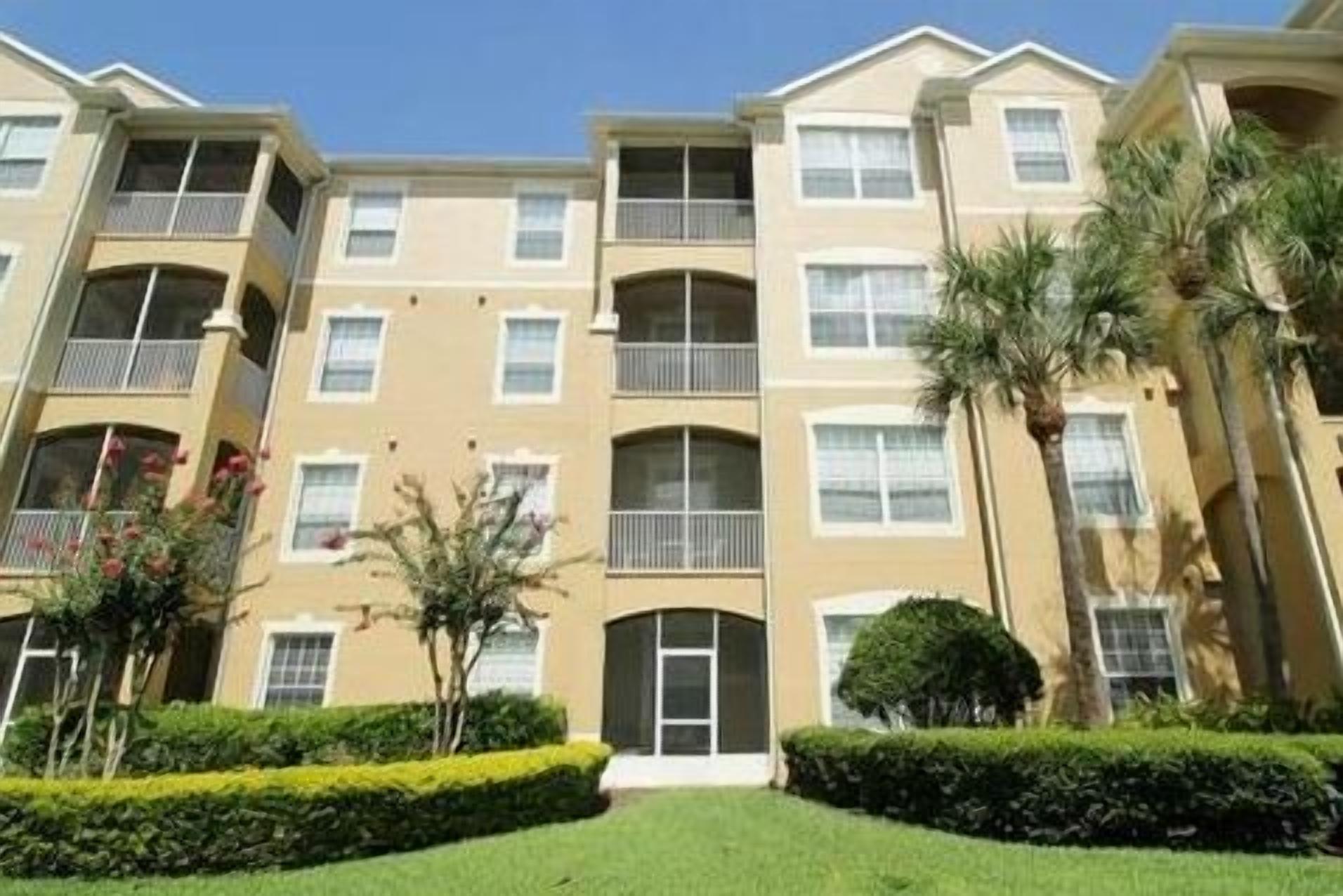 A multi-story residential building with balconies, a well-maintained lawn, and palm trees.