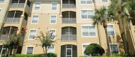A multi-story residential building with balconies, a well-maintained lawn, and palm trees.