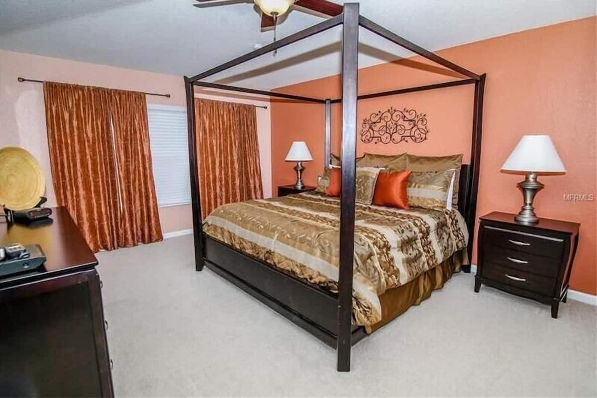 A four-poster bed with a patterned bedspread, two bedside lamps, and a nightstand with drawers.