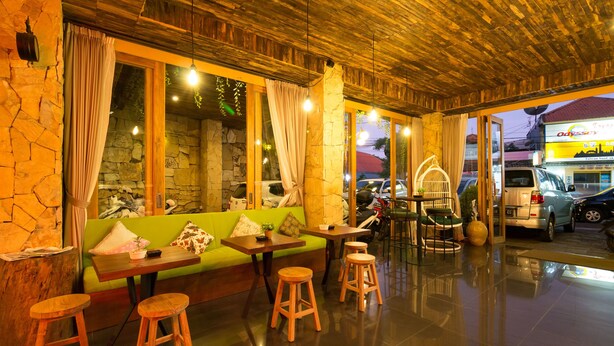 A restaurant with a wooden ceiling, stone walls, and a green sofa. There are wooden stools and a table with a fan. - Hadi Poetra Hotel (Kuta)