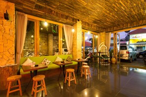 A restaurant with a wooden ceiling, stone walls, and a green sofa. There are wooden stools and a table with a fan. - Hadi Poetra Hotel (Kuta)