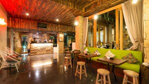 A restaurant with wooden ceiling, stone walls, and a green sofa. - Hadi Poetra Hotel (Kuta)