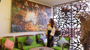 A room with green cushioned seating, a large abstract painting on the wall, and a decorative wooden panel. - Hadi Poetra Hotel (Kuta)