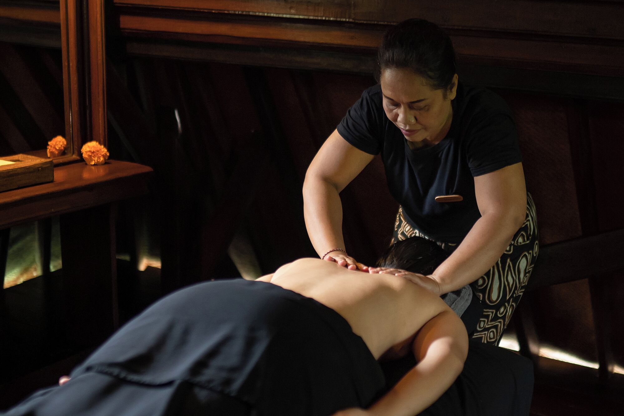Sessão de massagem em um ambiente com iluminação baixa e painéis de madeira.