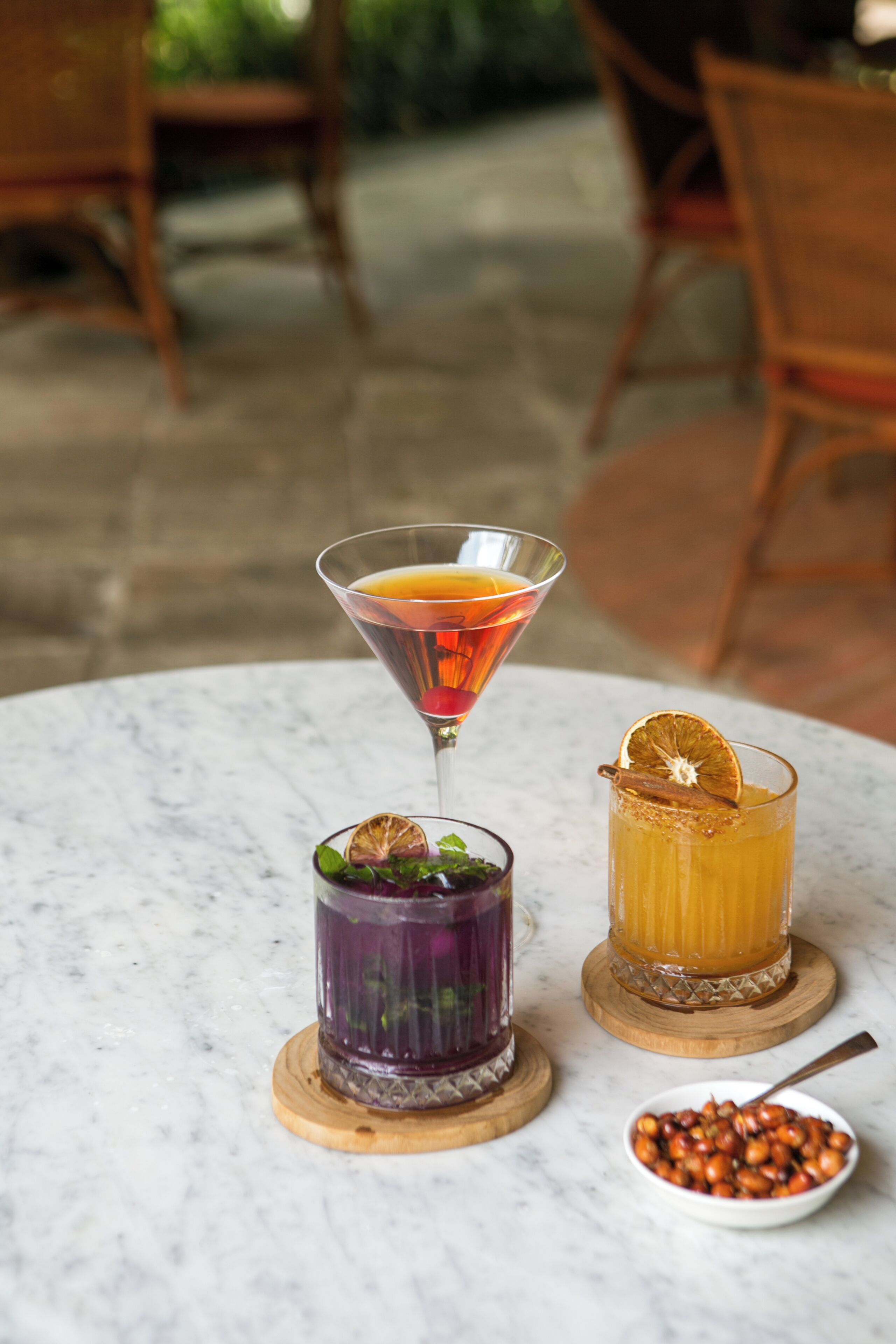 Three drinks on a marble table with a bowl of berries and a spoon.