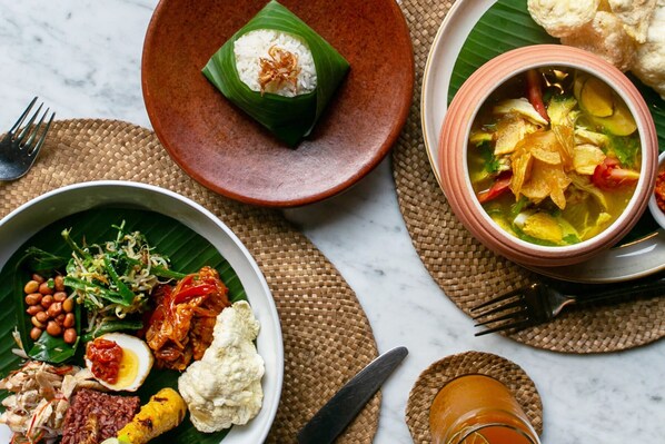 Variedad de platos sobre una mesa, incluyendo un tazón de sopa, un plato con arroz y verduras, y un plato con un huevo cocido y maní.