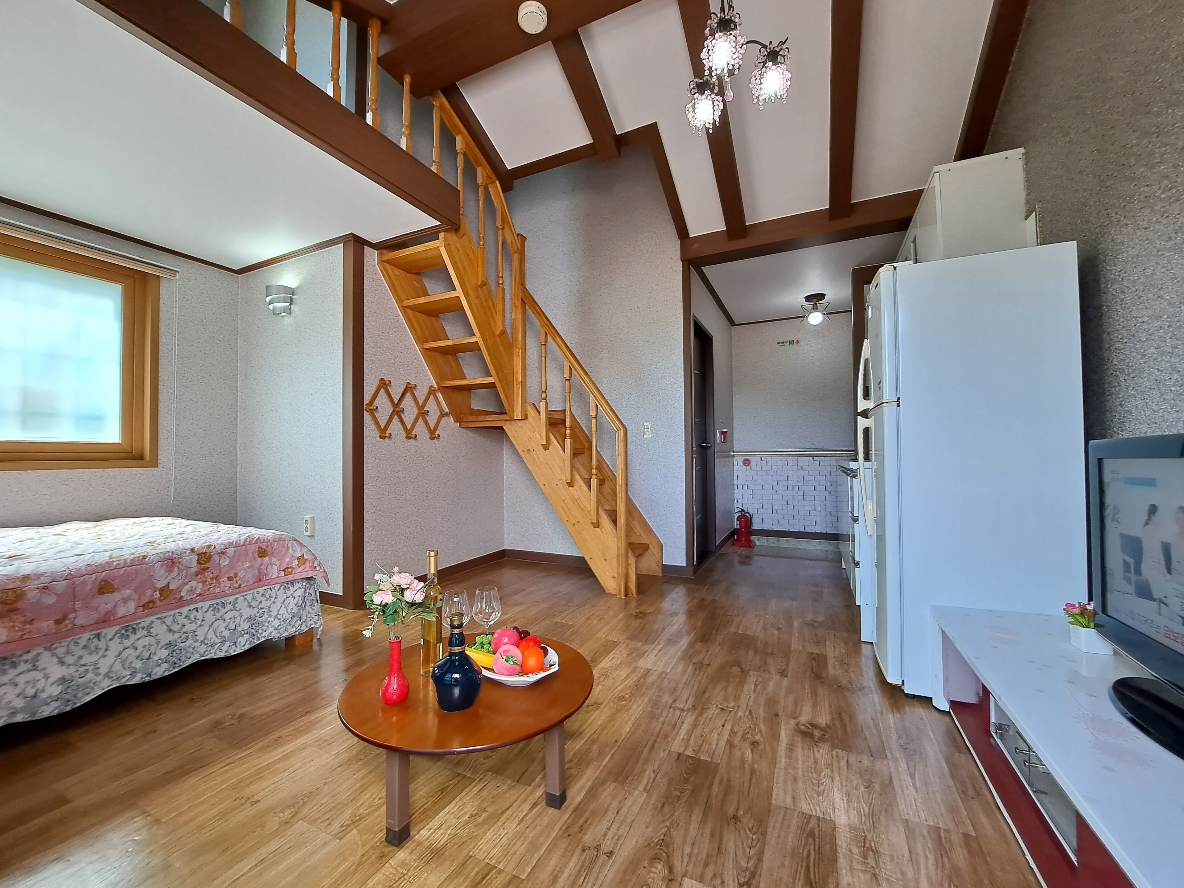 A compact living space with a wooden staircase, a dining table with fruit, and a kitchenette.