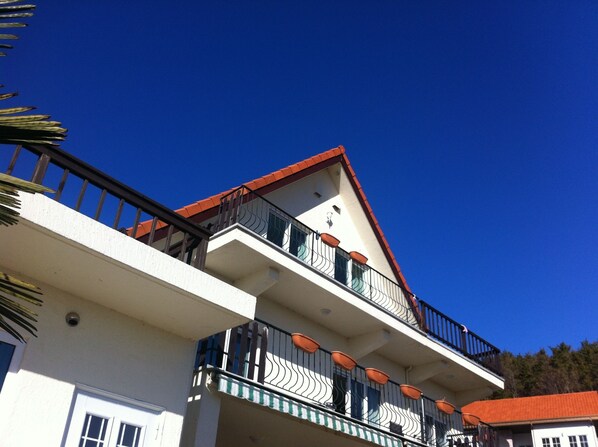 A multi-story building with balconies, a red roof, and a clear blue sky. - Namhae German Village Neuhaus in Korea (Namhae)