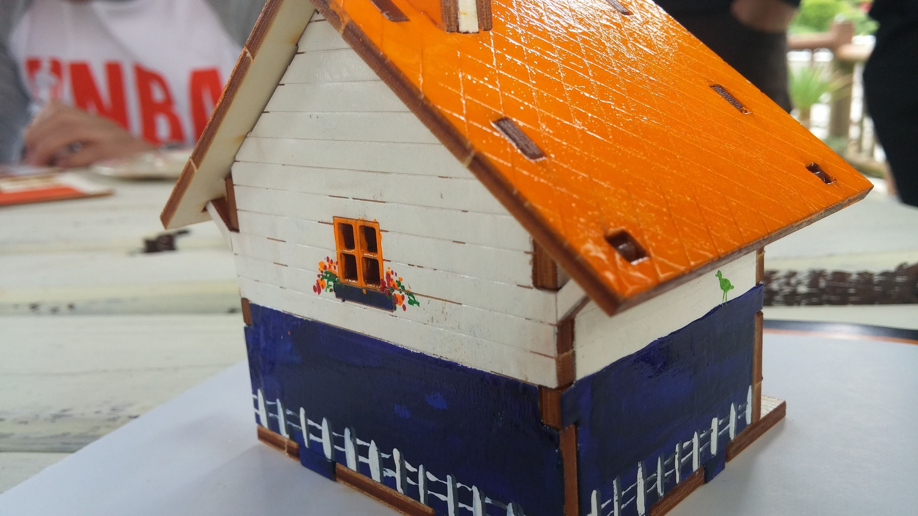 Ein Modellhaus mit weißem Oberteil, blauem Unterteil und einem orangefarbenen Dach.