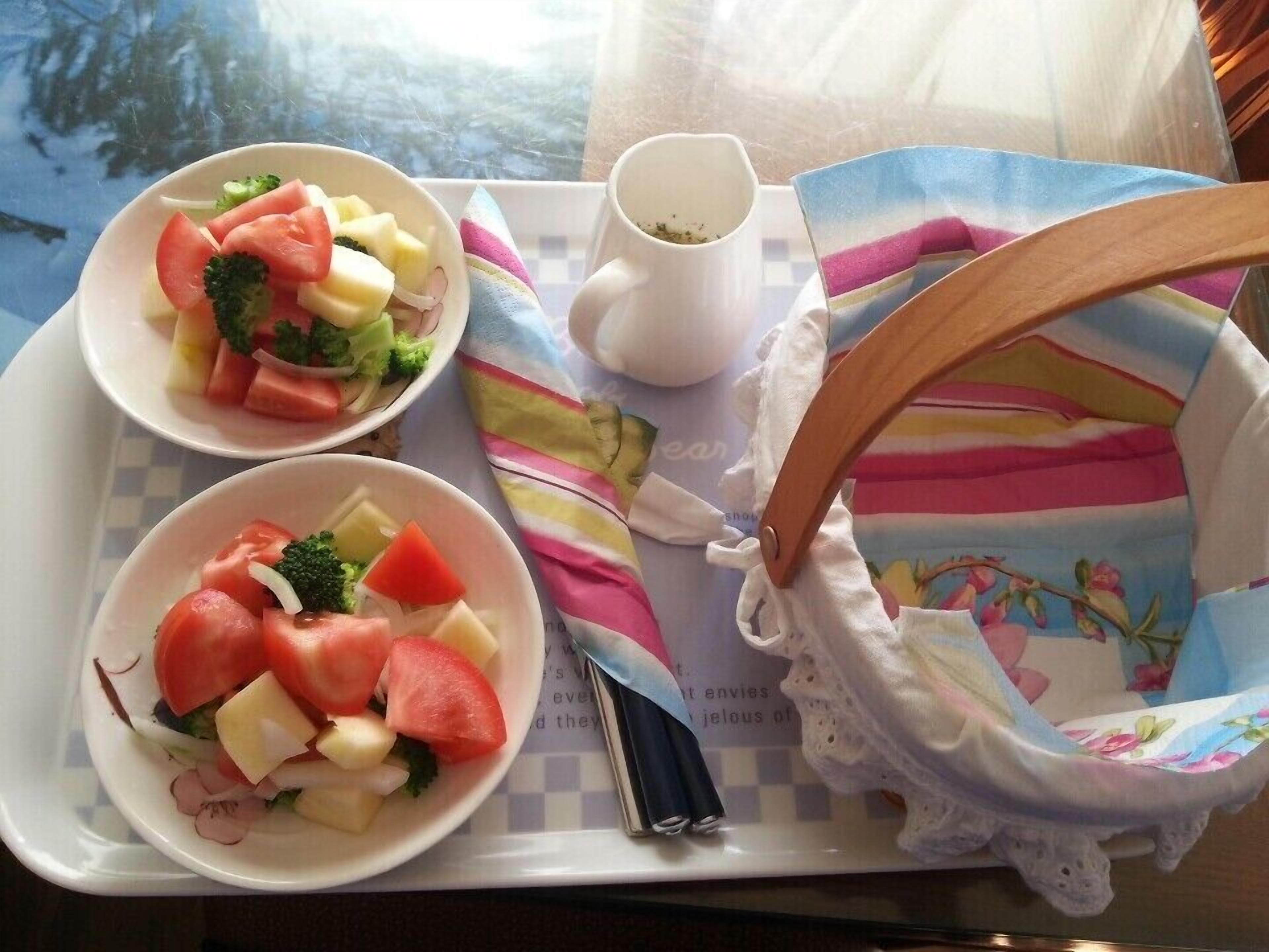 A tray with two bowls of fruit salad and a white cup, placed on a table with a colorful cloth and a small white bag.