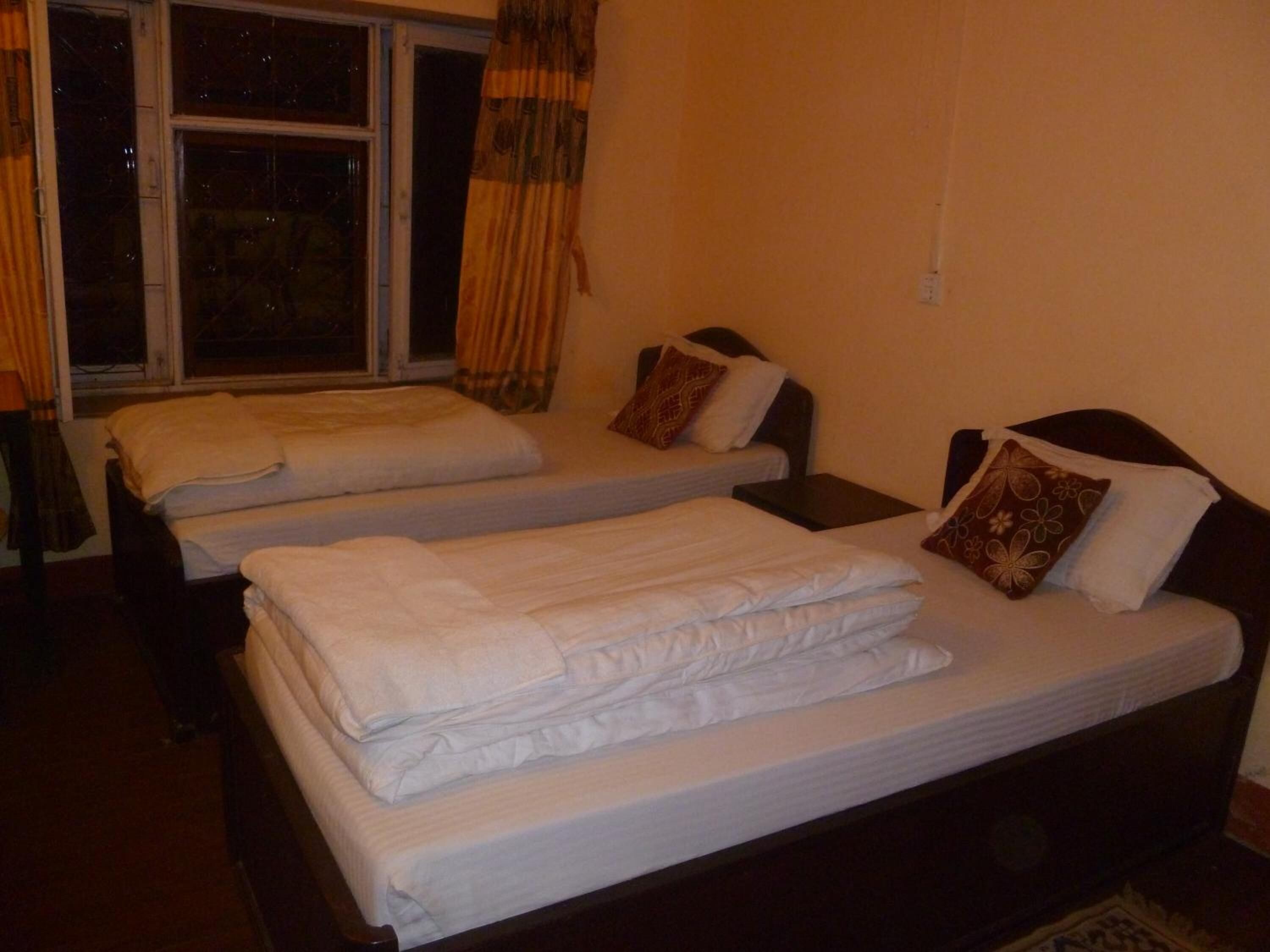 A hotel room with two single beds, a window with curtains, and a bedside table with a lamp.