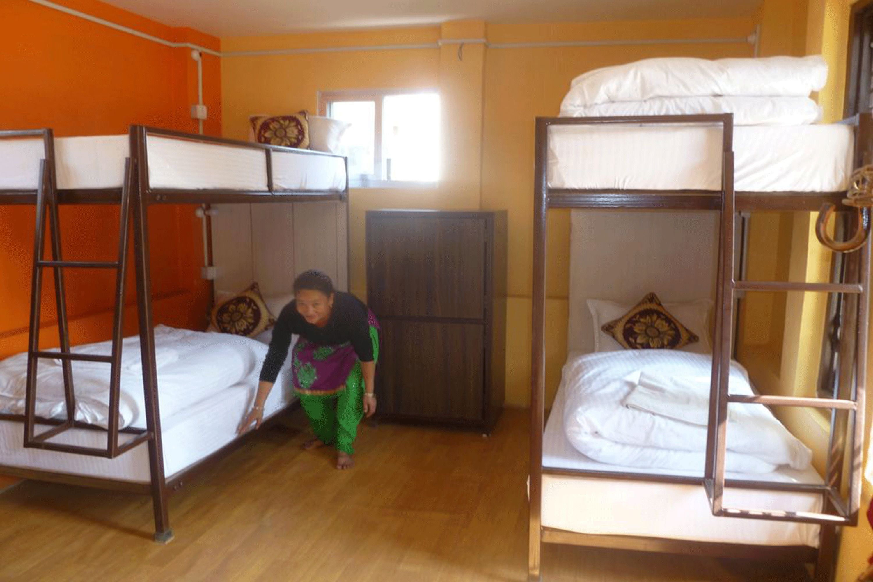 A room with bunk beds, wooden flooring, and a window providing natural light.