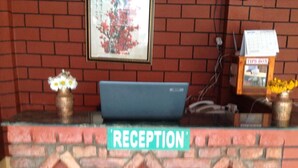A reception desk with a 'RECEPTION' sign, a laptop, a calendar, and a vase with flowers. - Andes House (Kathmandu)