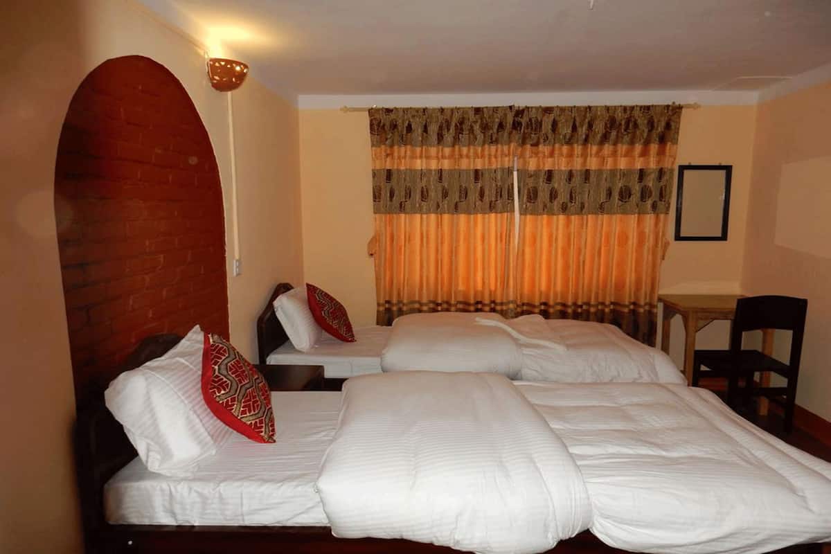 A hotel room with two single beds, a wooden desk, a chair, and a brick archway.