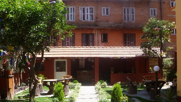 A courtyard with a brick building, potted plants, and outdoor seating. - Andes House (Kathmandu)