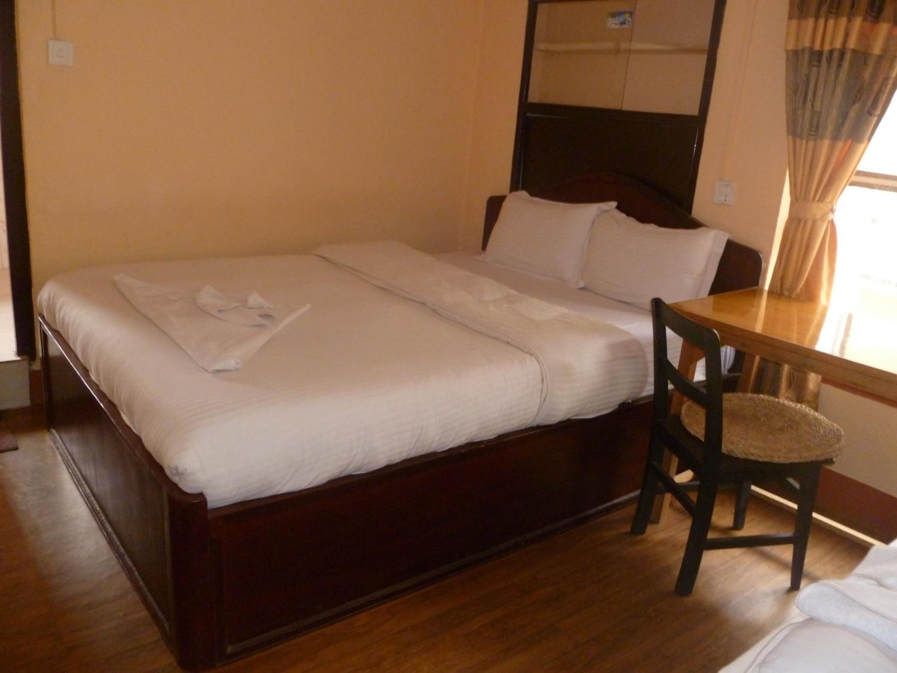 A single bed with a wooden frame, a small table with a chair, and a mirror above the bed.