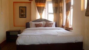 A neatly made bed with white linens and patterned pillows, a wooden headboard, and a window with curtains. - Andes House (Kathmandu)