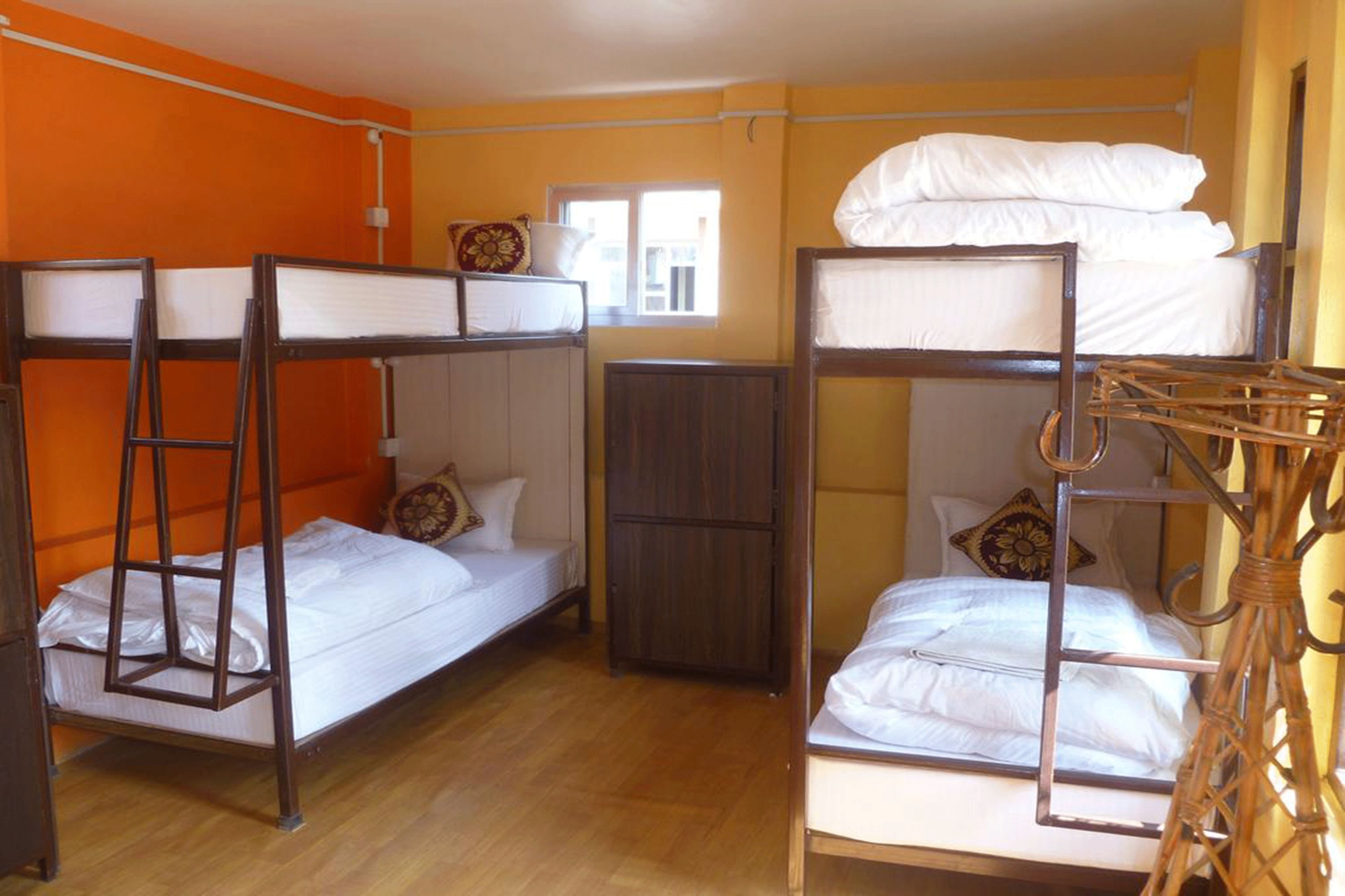 A dormitory room with bunk beds, wooden furniture, and a window providing natural light.