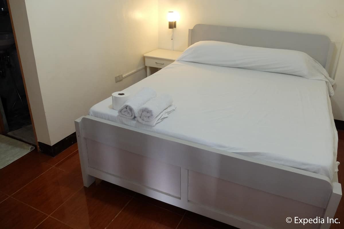 Una cama bien hecha con sábanas y toallas blancas, una mesita de noche con lámpara y un enchufe de pared.