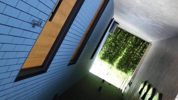 A corridor with a blue tiled wall, a wooden door, and a view of greenery outside.