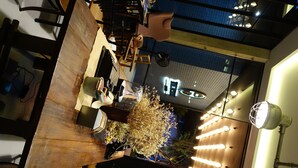 A modern interior with a wooden reception desk, a seating area with chairs, and a decorative plant. - The Restro (Hua Hin)