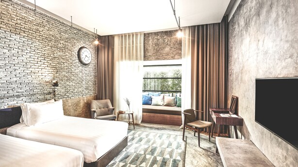 A modern hotel room with a brick wall, a large bed, a desk, a chair, and a TV. - The Restro (Hua Hin)