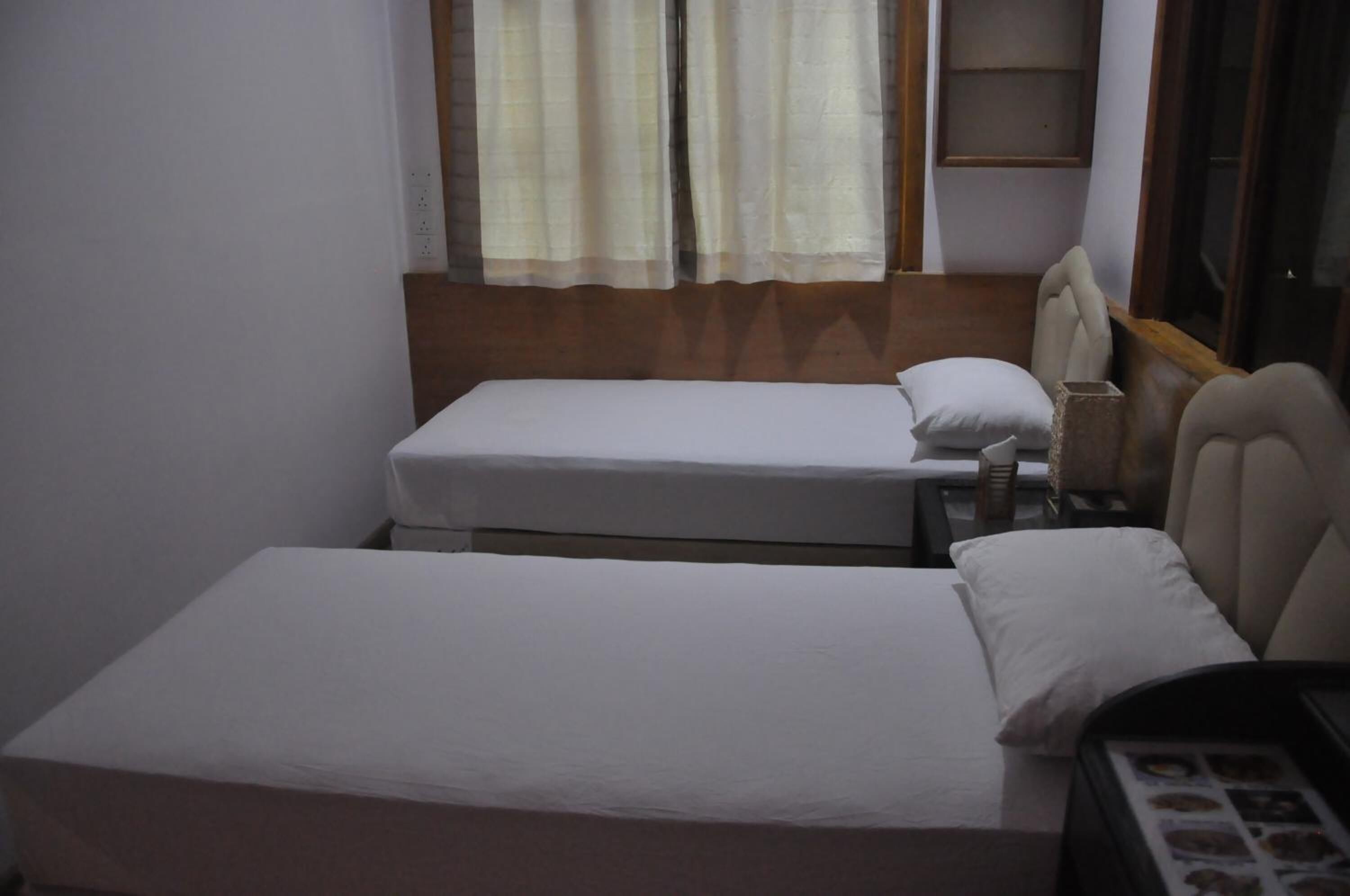 Habitació petita i senzilla amb dos llits, una tauleta de nit i una finestra amb cortines.