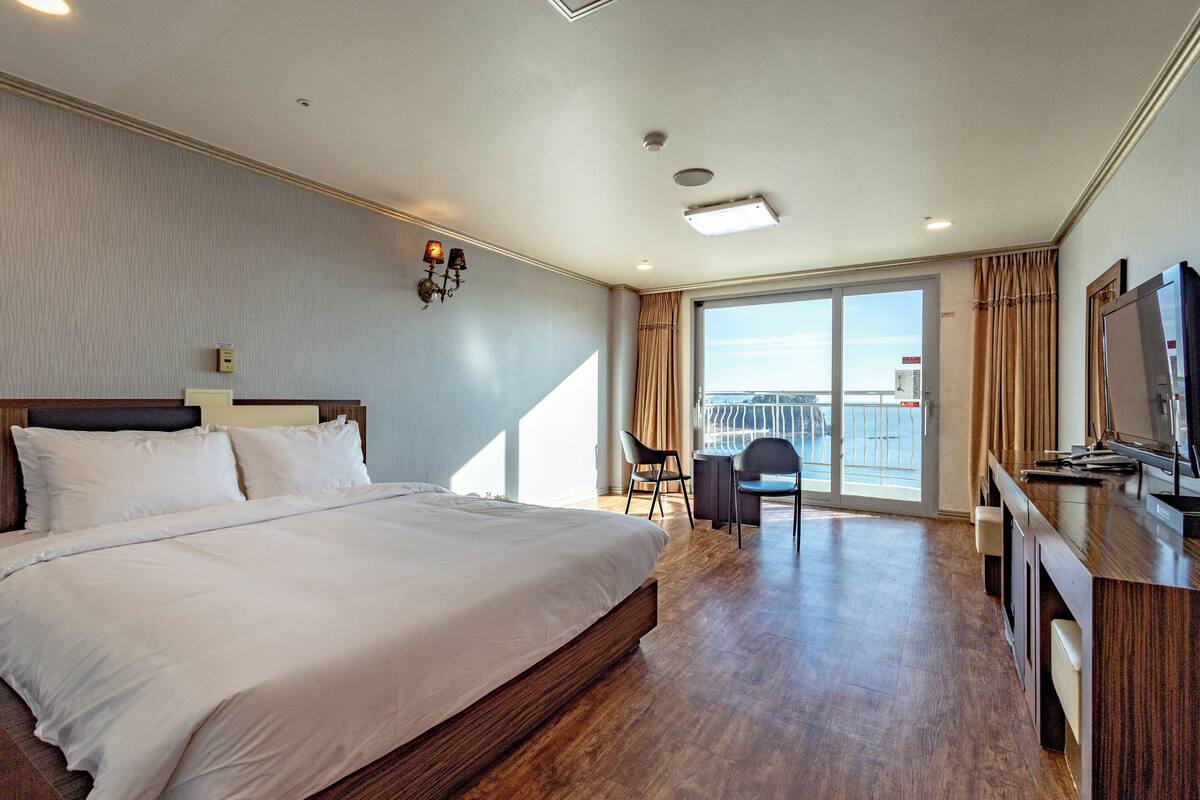 Una habitación de hotel con una cama grande, un escritorio con televisor y un balcón con vistas.