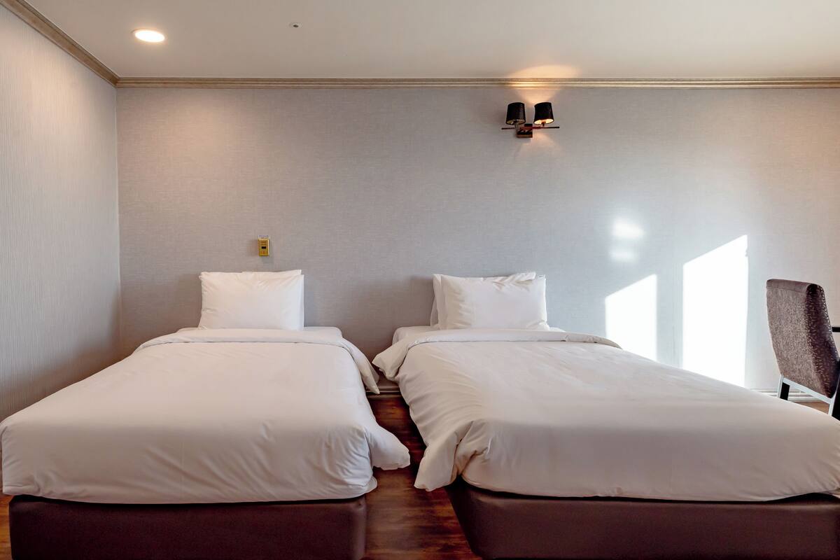 Una habitación de hotel con dos camas individuales, una mesita pequeña y una silla.