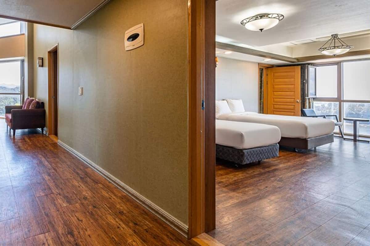 Habitación de hotel con piso de madera, un ventanal grande, cama y escritorio.