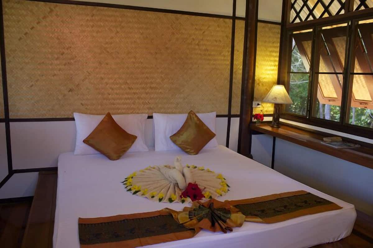 A neatly made bed with a decorative centerpiece, a wooden headboard, and a window with a view of greenery.