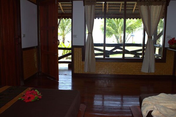 A room with a wooden floor, a bed, a window with curtains, and a view of palm trees outside. - Libong Relax Beach Resort (Ko Libong)
