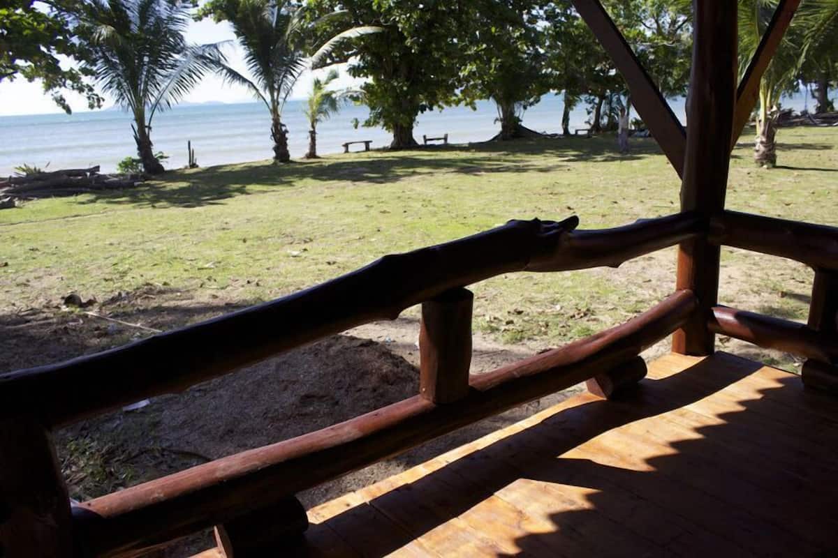A wooden deck with a view of a grassy area and palm trees, overlooking a body of water.