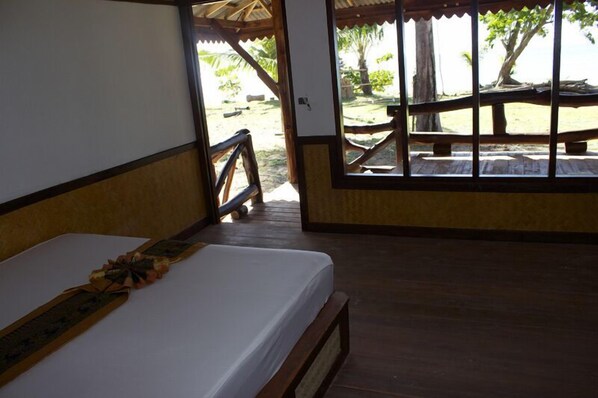 A room with a bed, wooden floor, and a view of a beach with a wooden deck and palm trees. - Libong Relax Beach Resort (Ko Libong)