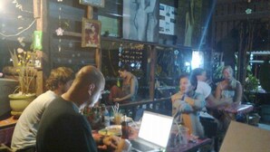 A restaurant with tables and chairs, some people sitting and others standing. There are plants and pictures on the walls. - ABC Bungalow (Ko Pha-ngan)