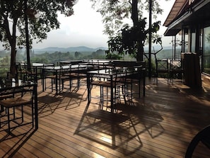 An outdoor wooden deck with tables and chairs, surrounded by trees and overlooking a mountainous landscape. - Rabbiz Hill Resort (Kaeng Hang Maeo)
