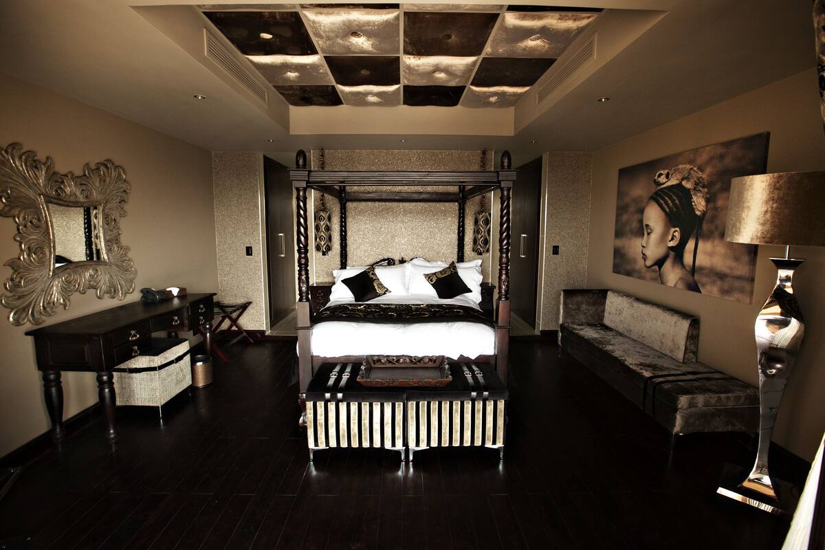 A luxurious bedroom with a large bed, a decorative mirror, a sofa, and a unique ceiling design.