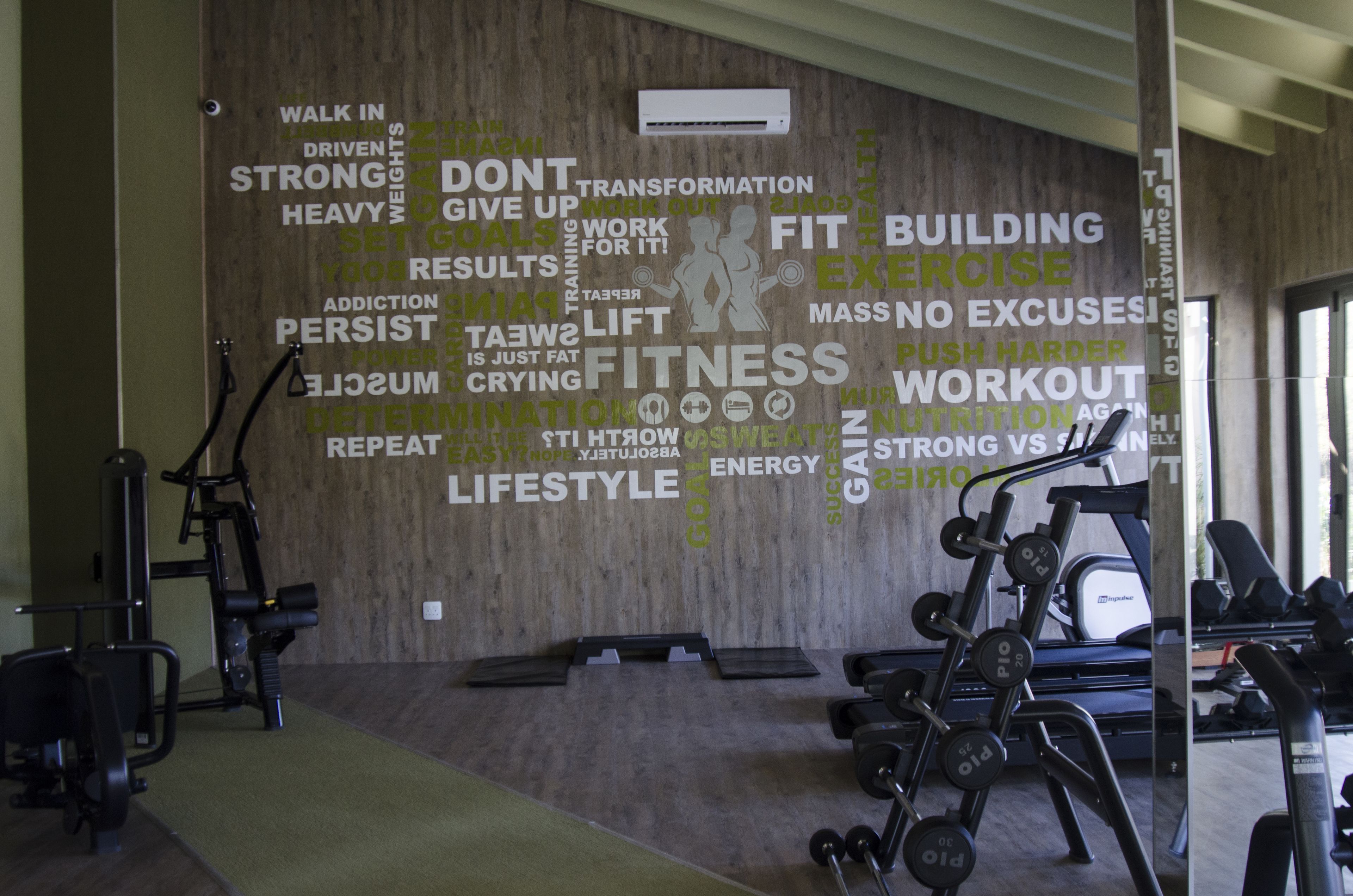 A gym with a motivational word cloud on the wall, various exercise equipment, and a treadmill.