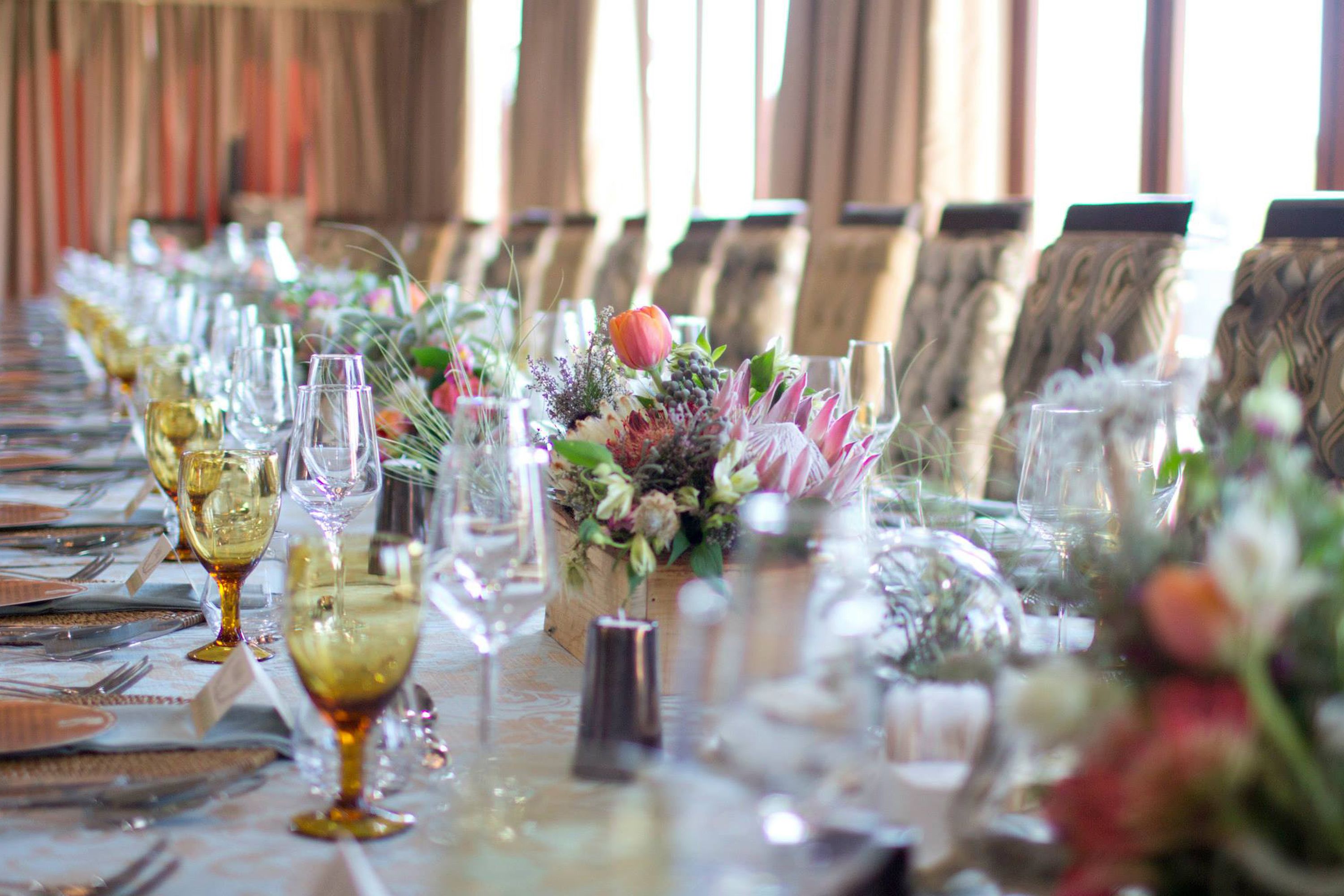 A long dining table set with wine glasses, plates, and floral centerpieces.