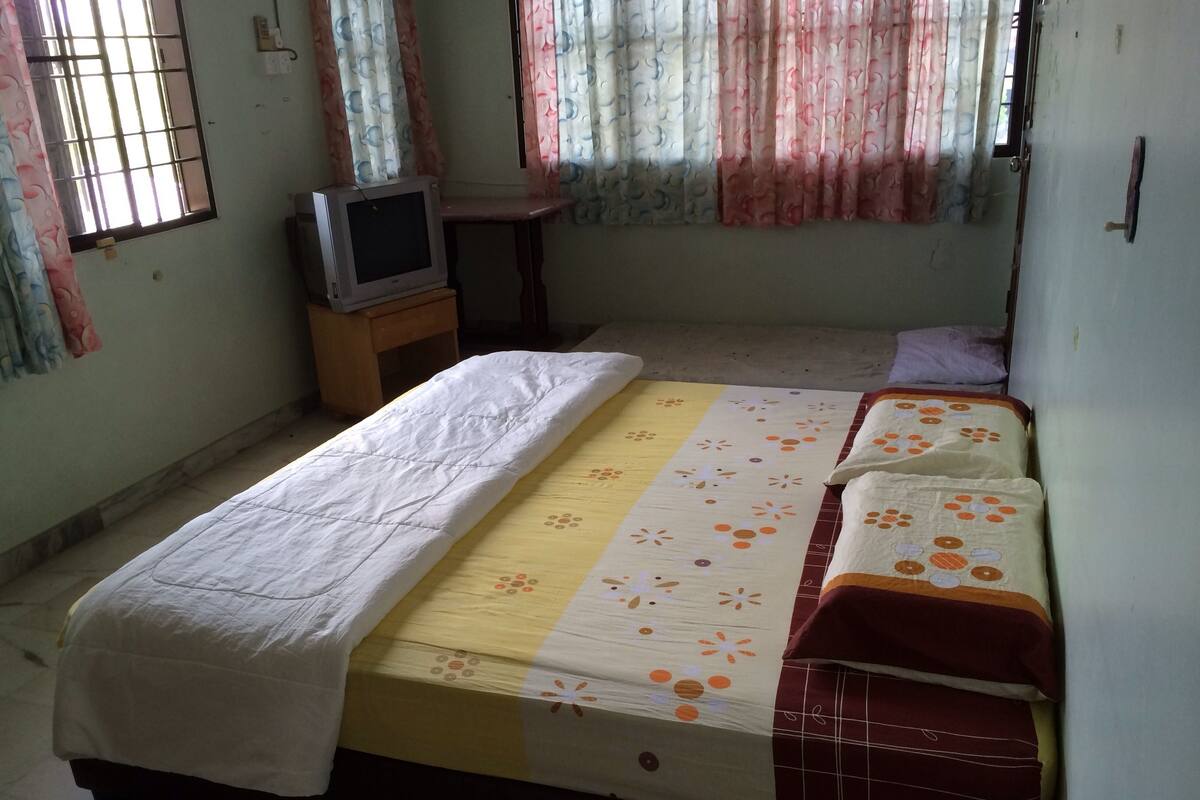 A bedroom with a bed, a TV on a small table, and curtains.