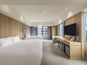 Habitación de hotel con dos camas, un escritorio, un televisor y un ventanal grande.