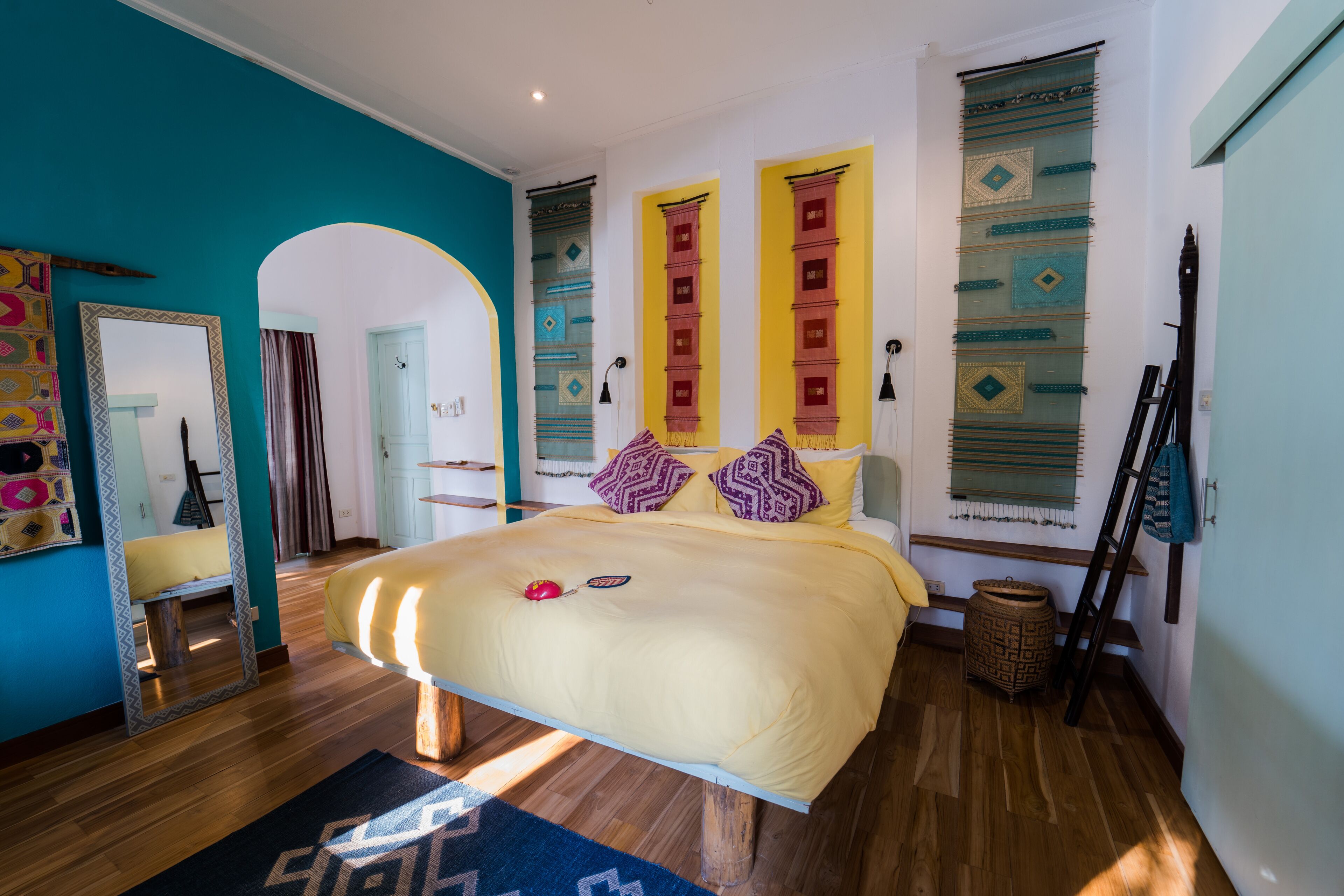 A bedroom with a large bed, wooden flooring, a mirror, and decorative pillows.