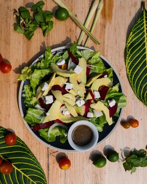 A salad with various vegetables and cheese on a plate, surrounded by tomatoes, limes, and mint leaves on a wooden table. - Ock Pop Tok Mekong Villa (Luang Prabang)