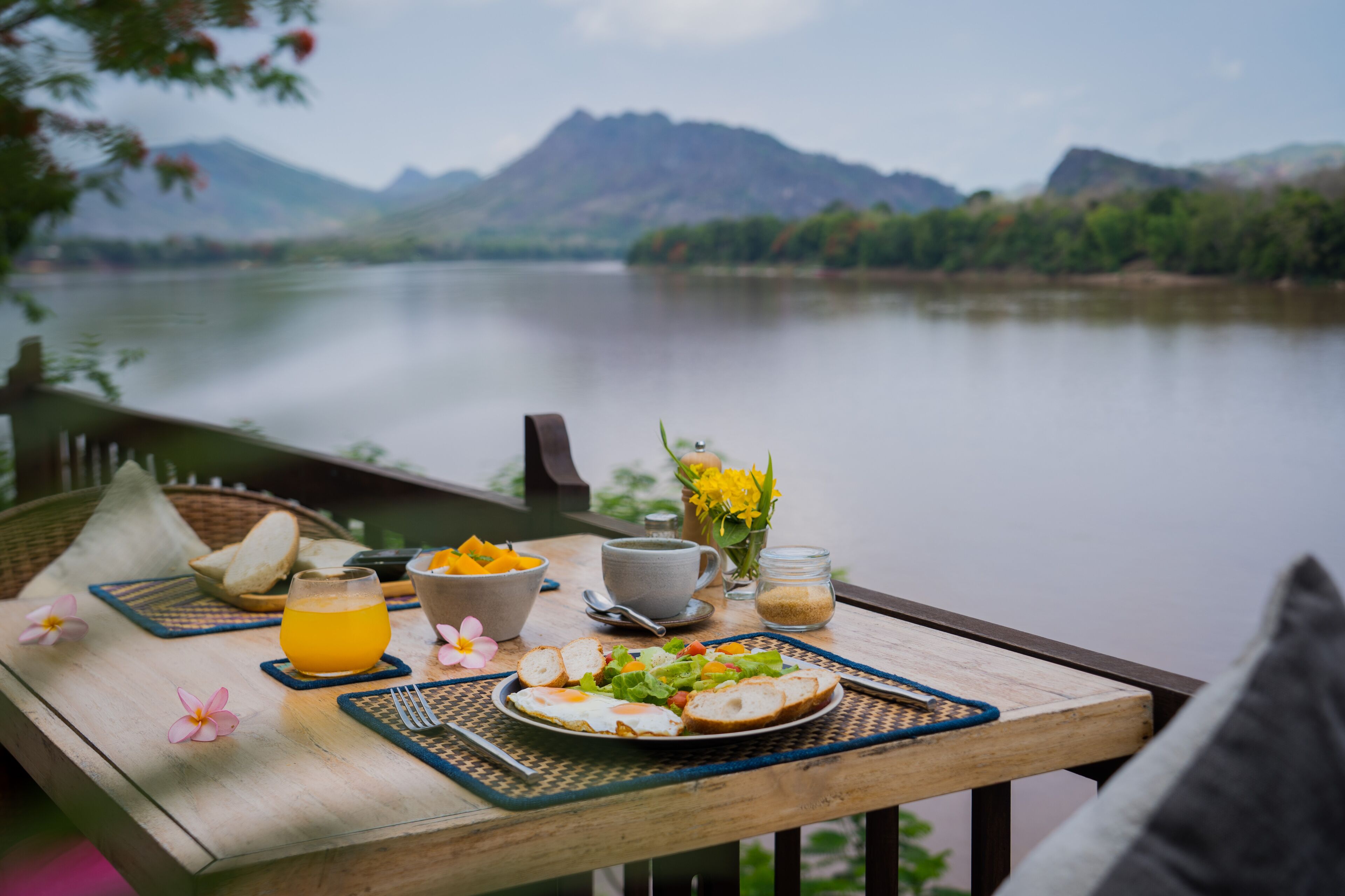 A wooden table with breakfast items and a view of a lake and mountains.