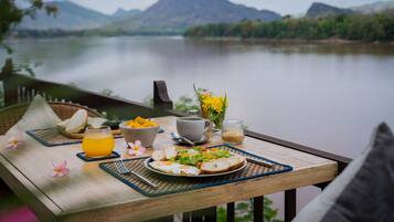 Una mesa de madera con alimentos para el desayuno y vistas a un lago y montañas.