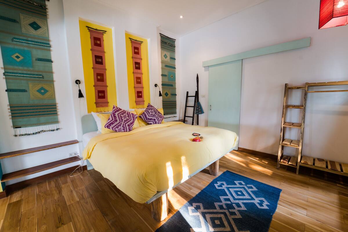 A bedroom with a bed, wooden floor, and a blue patterned rug.